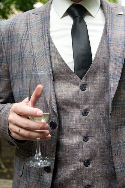 Un hombre con un traje de tres piezas sostiene una copa Para cerrar La mano de un hombre sostiene una copa de vino blanco