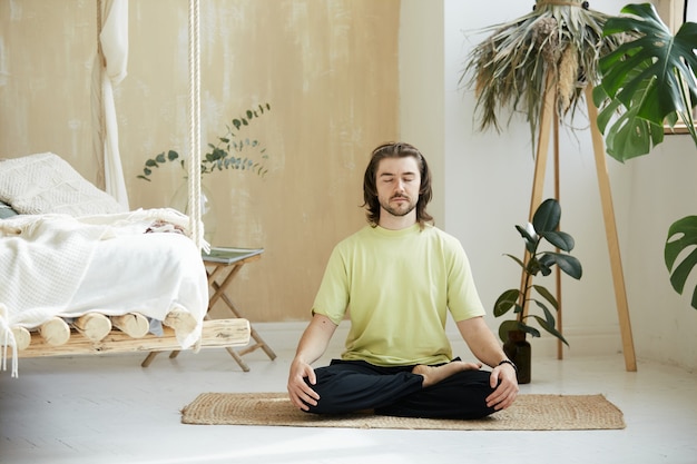 Hombre tranquilo sentado en casa en pose de meditación, hombre guapo en lotus asna concentrándose en la respiración, concepto de atención plena