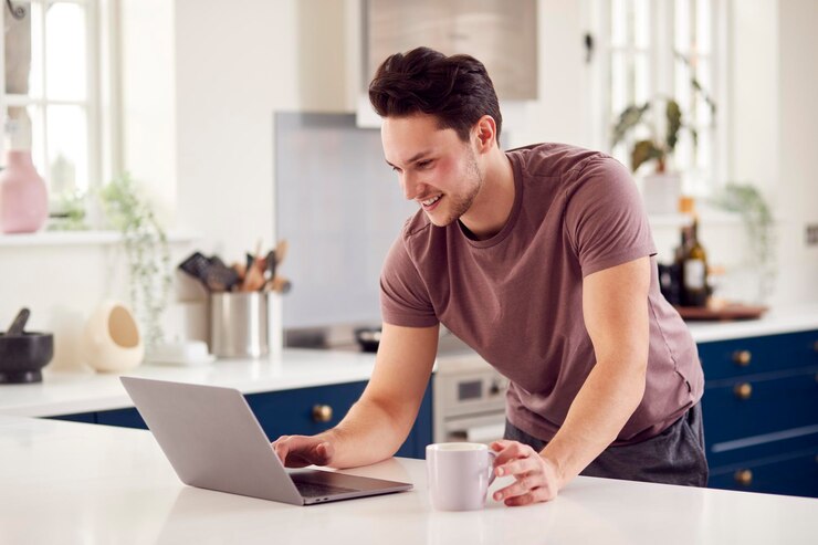 Foto hombre transgénero trabajando desde casa mirando la computadora portátil en el mostrador de la cocina