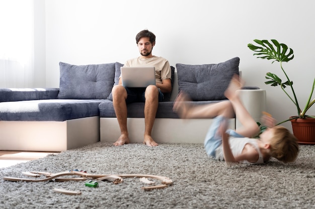 Hombre tratando de trabajar en la computadora portátil desde casa mientras sus hijos corren