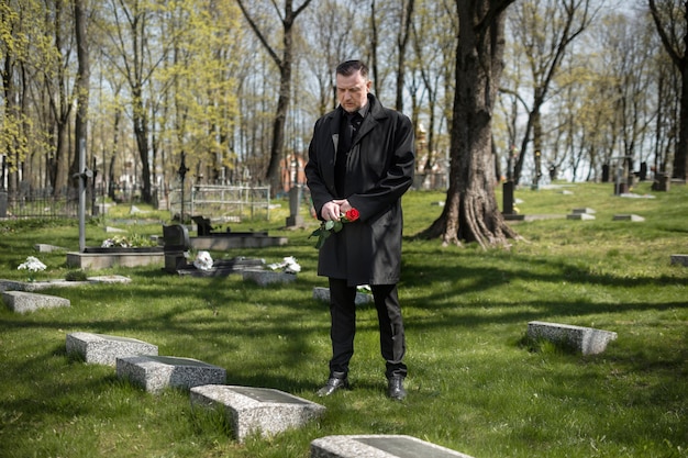 Foto hombre trayendo una rosa a una lápida en el cementerio