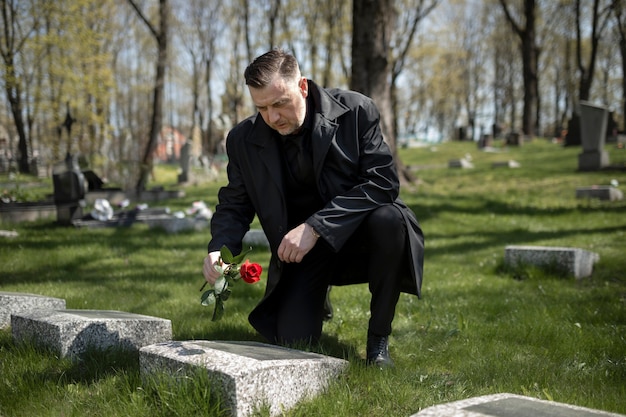 Foto hombre trayendo una rosa a una lápida en el cementerio