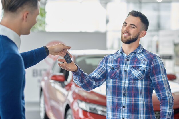 Hombre trigueno feliz que toma llave del encargado en salón del coche.