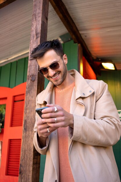 Hombre en trinchera beige usando un teléfono inteligente al aire libre