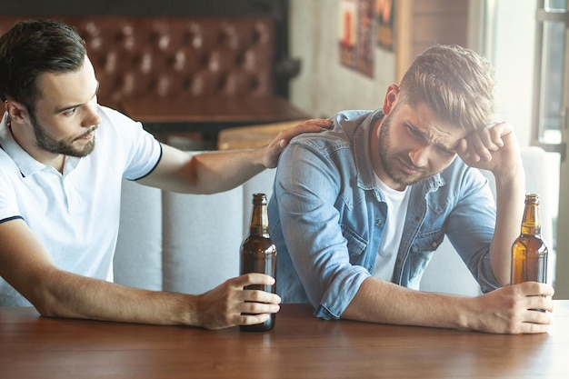 Hombre triste bebiendo cerveza a su amigo en el café