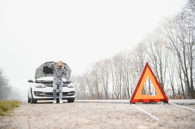 Hombre triste en el camino al lado del auto roto