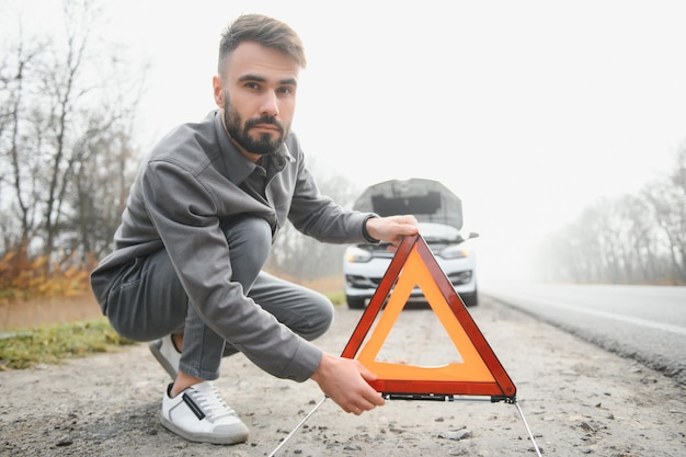 Hombre triste en el camino al lado del auto roto