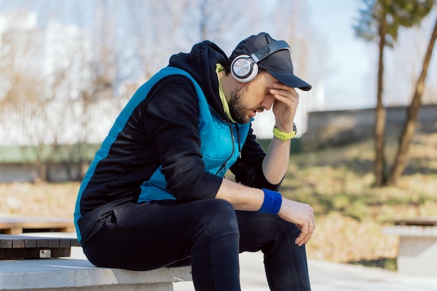 Un hombre triste y cansado no está contento con los resultados del entrenamiento. El corredor descansa en una pared en el parque.