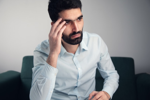 Hombre triste con la mano en la cabeza sentado en el sofá