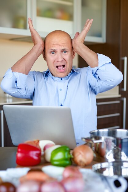 Foto hombre triste mirando receta en la computadora portátil en la cocina de casa