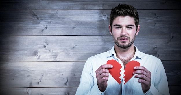 Foto hombre triste que sostiene las mitades del corazón contra el fondo de tablones de madera blanqueada