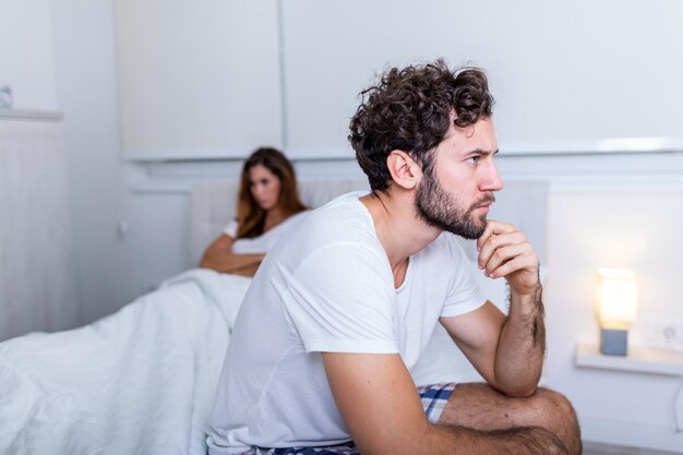 Foto hombre triste y reflexivo después de discutir con su novia dificultades en la relación conflicto y concepto familiar pareja infeliz con problemas en el dormitorio hombre triste sentado en la cama amiga en el fondo