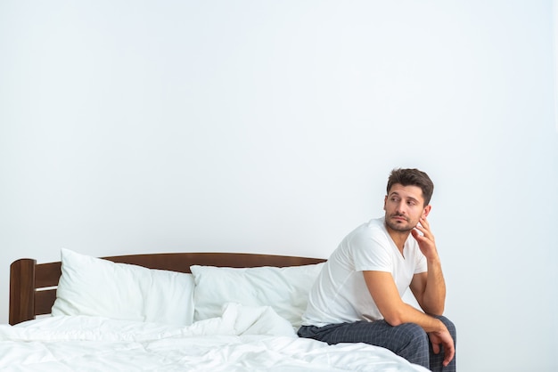 El hombre triste sentado en la cama sobre el fondo blanco.