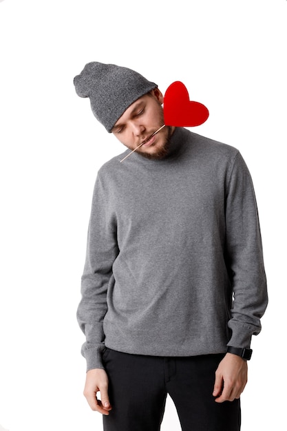 Hombre triste con sombrero gris con corazón de papel rojo aislado sobre fondo blanco.