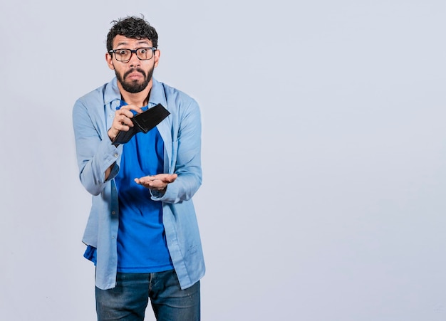 Hombre triste sosteniendo la billetera vacía y mirando a la cámara Hombre infeliz y sorprendido mirando una billetera vacía Persona viendo su billetera vacía Hombre con problemas financieros