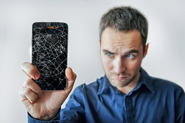 Hombre triste tiene teléfono inteligente roto. Pantalla de teléfono rota. No funciona el teléfono