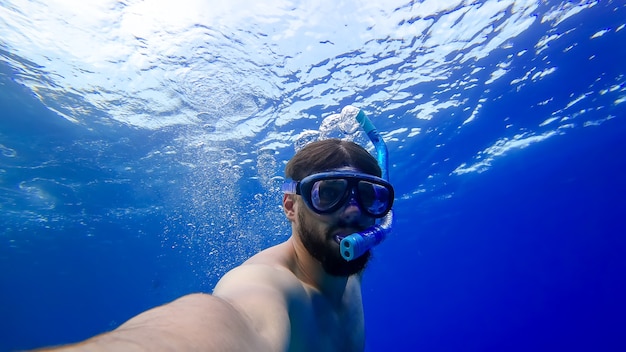 Un hombre con tubos de respiración y máscaras se sumerge en el fondo del mar rojo.Un hombre barbudo se dedica a bucear.