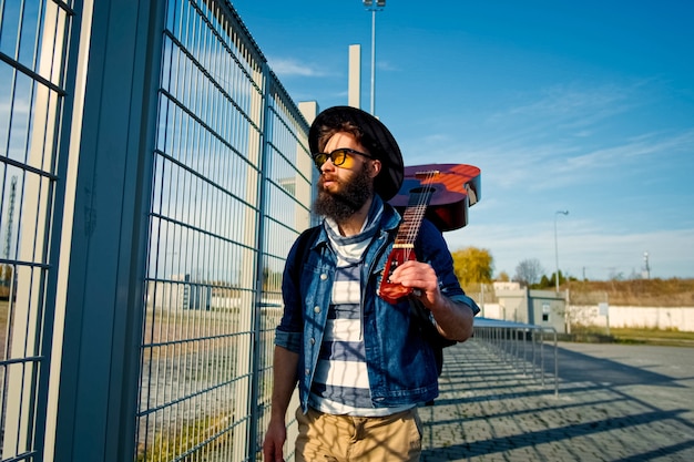 Hombre de turismo con mochila y sombrero de turista sosteniendo una guitarra