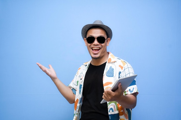 Foto hombre turista asiático sonriente sosteniendo una tableta digital y señalando con el dedo a la tableta digital