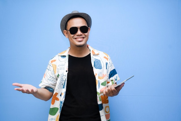 Foto hombre turista asiático sonriente sosteniendo una tableta digital y señalando con el dedo a la tableta digital