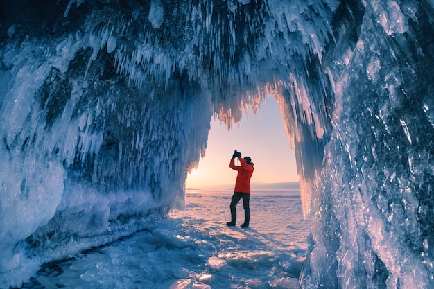 Hombre turista fotografía la cueva de hielo en el lago Baikal al atardecer Paisaje invernal de Baikal Rusia