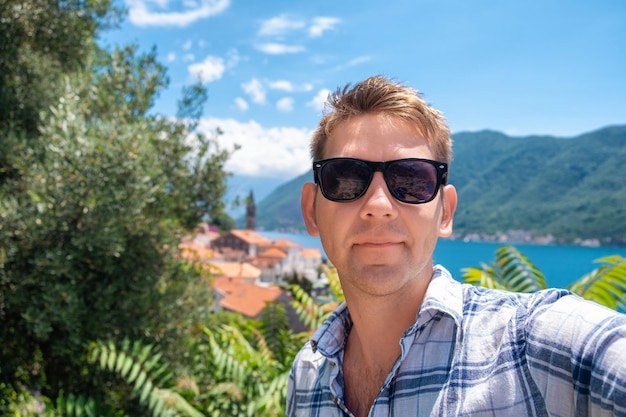 Hombre turista con gafas de sol toma una selfie con la ciudad vieja de Perast en la bahía de Kotor Montenegro en el fondo