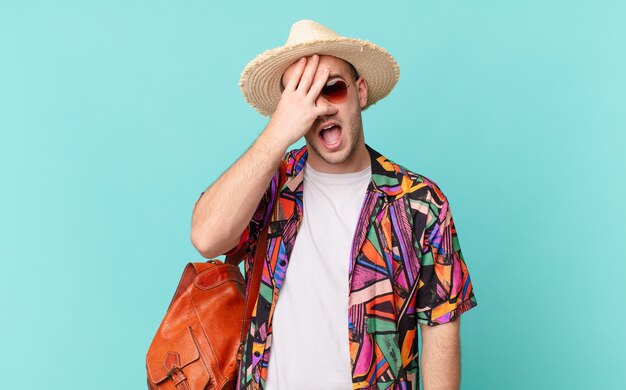 Hombre turista mirando conmocionado, asustado o aterrorizado, cubriéndose la cara con la mano y mirando entre los dedos