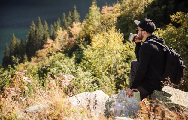 Hombre turista relajándose en la cima de una colina, observando maravillosos paisajes de montañas y lagos.