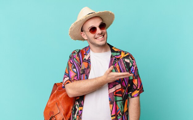 Hombre turista sonriendo alegremente, sintiéndose feliz y mostrando un concepto en el espacio de la copia con la palma de la mano