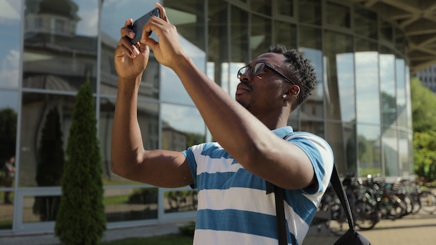 Hombre turista tomando fotos con teléfono con cámara fuera del joven afroamericano tomando fotos en el teléfono en la calle