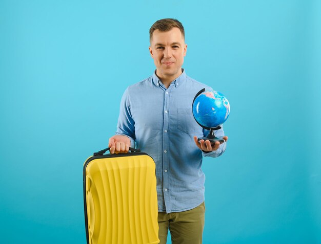 Hombre de turista viajero emocionado aislado sobre fondo azul. Pasajero que viaja al exterior los fines de semana. Concepto de viaje de vuelo aéreo. Sosteniendo el globo del mundo.