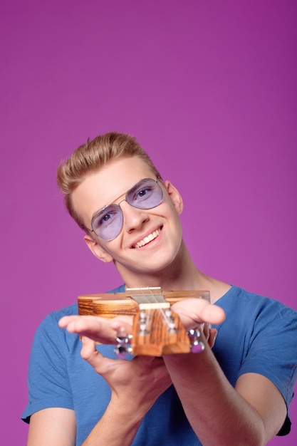 Hombre con ukelele en manos sobre fondo púrpura