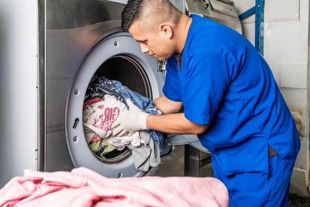 Hombre uniformado poniendo un montón de ropa en una lavadora industrial