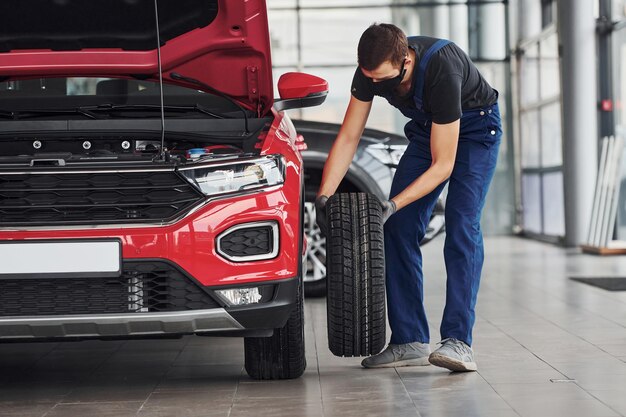 Hombre en uniforme cambiando neumático de automóvil Concepción de servicio de automóvil