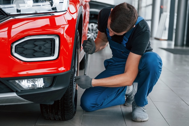 Hombre en uniforme cambiando el neumático del automóvil. Concepción del servicio de coche.