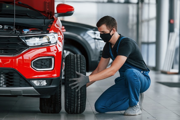 Hombre en uniforme cambiando el neumático del automóvil. Concepción del servicio de coche.