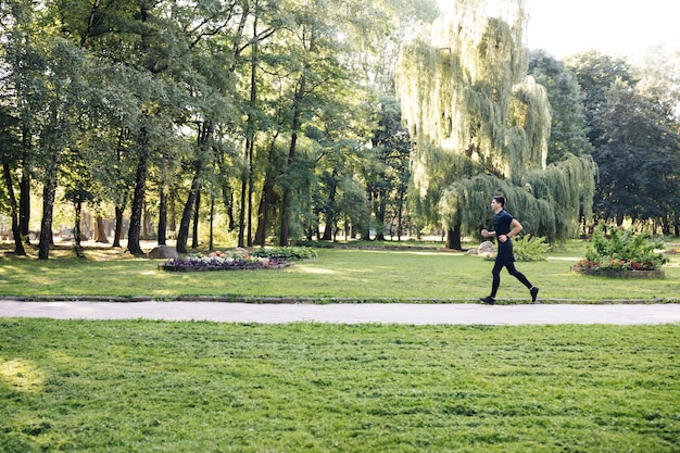 Hombre en uniforme deportivo de verano corriendo en el parque de la ciudad con reloj inteligente para medir la velocidad