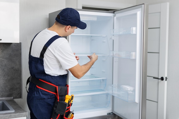 Foto hombre en uniforme con herramientas está reparando un refrigerador en la cocina