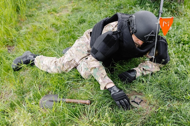 Un hombre con uniforme militar y chaleco antibalas trabaja en el bosque para desminar el territorio Un hombre advierte del peligro haciendo una marca roja