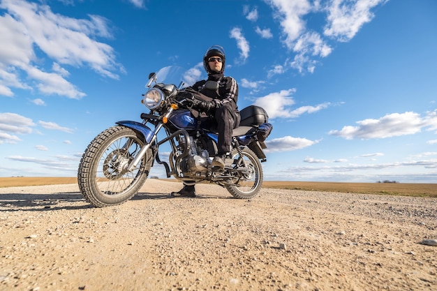 Hombre con uniforme negro en bicicleta con el telón de fondo del panorama del concepto de viaje en motocicleta de campo y cielo azul