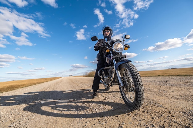 Hombre con uniforme negro en bicicleta con el telón de fondo del panorama del concepto de viaje en motocicleta de campo y cielo azul