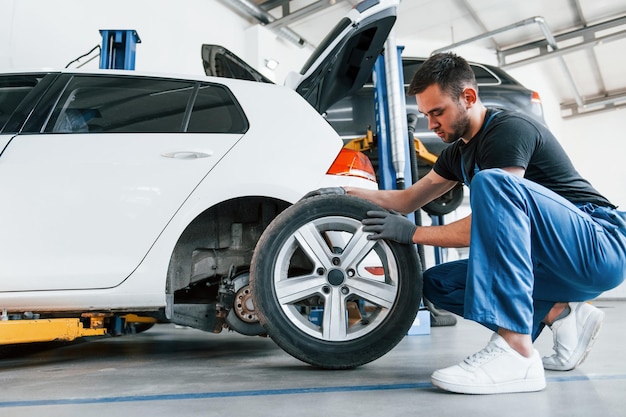 Hombre en uniforme de trabajo cambiando la rueda del coche en el interior Concepción del servicio de automóviles