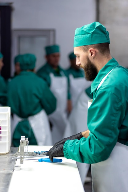 Un hombre con uniforme verde está trabajando en una mesa con una caja azul y una botella de líquido.