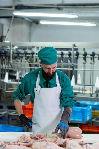 Un hombre con uniforme verde se para en una fábrica con un contenedor azul al fondo.