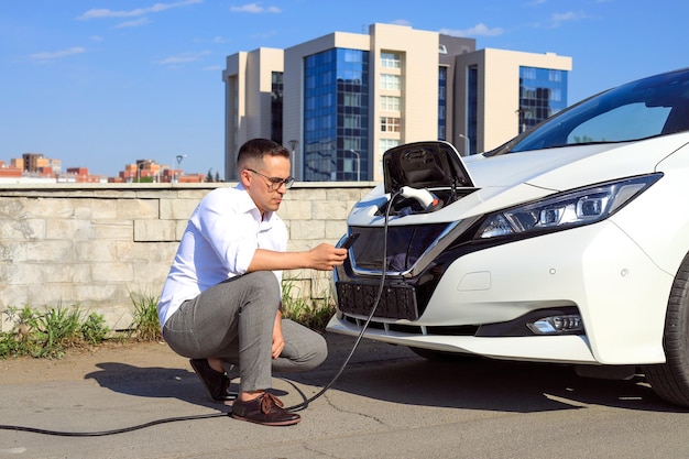 Un hombre usa una aplicación en su teléfono para cargar un auto eléctrico en el concepto de energía verde y ecoenergía destinada a reducir las emisiones de CO2