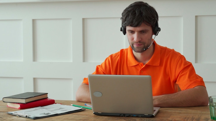Foto el hombre usa un auricular para hablar en línea en su lugar de trabajo, el hombre confiado se sienta en el escritorio de la oficina y mira la pantalla del portátil