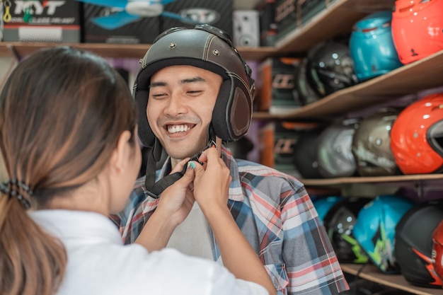 El hombre usa un casco con la ayuda de un dependiente al colocar la hebilla de la correa contra el fondo del estante de exhibición del casco