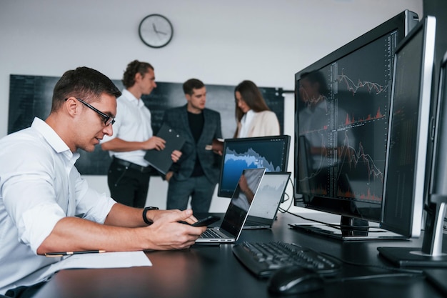 El hombre usa una computadora portátil El equipo de corredores de bolsa trabaja en una oficina moderna con muchas pantallas