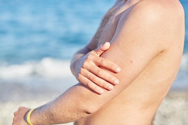 El hombre usa crema solar para un bronceado seguro con alto SPF en la playa Cerrar Foto de alta calidad