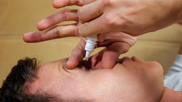 El hombre usa gotas para los ojos recostado en el sofá en la sala de estar